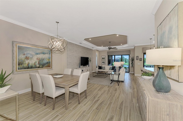 dining area featuring light hardwood / wood-style floors, ceiling fan with notable chandelier, a raised ceiling, and ornamental molding