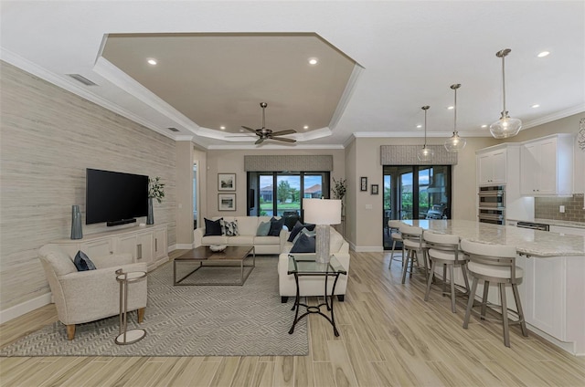 living room featuring ornamental molding, ceiling fan, a tray ceiling, and light hardwood / wood-style floors