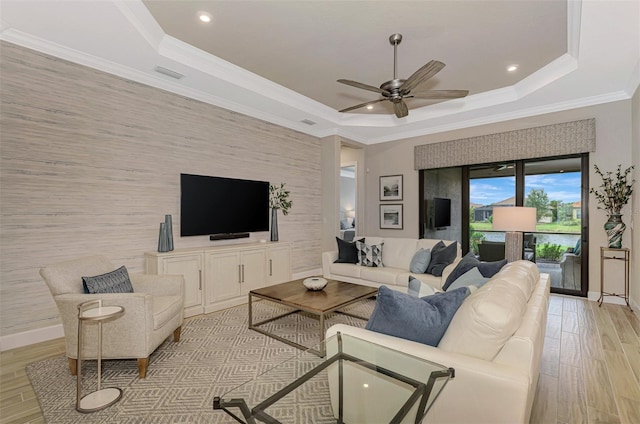 living room with light hardwood / wood-style flooring, ceiling fan, crown molding, and a tray ceiling