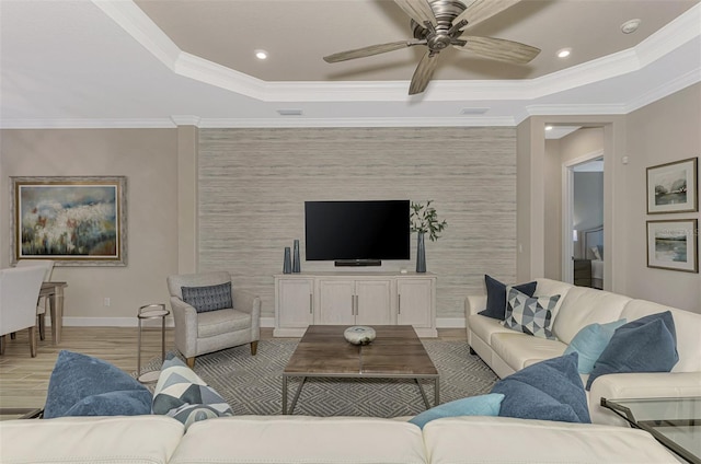 living room featuring ceiling fan, a raised ceiling, light wood-type flooring, and ornamental molding