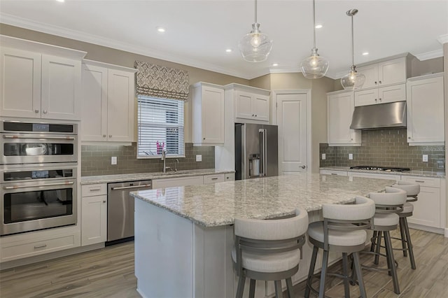 kitchen featuring stainless steel appliances, pendant lighting, tasteful backsplash, a kitchen island, and white cabinetry