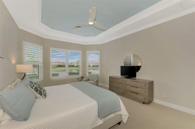 carpeted bedroom with ceiling fan, multiple windows, a tray ceiling, and ornamental molding