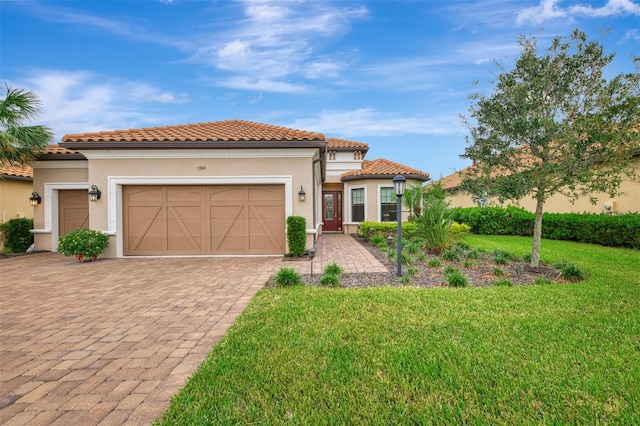 mediterranean / spanish-style home featuring a garage, decorative driveway, a front lawn, stucco siding, and a tile roof