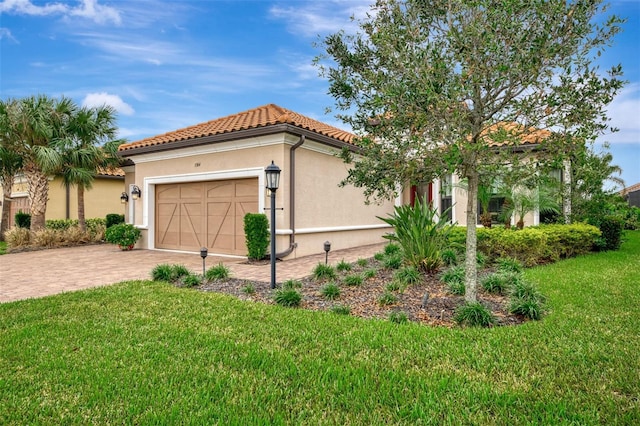 view of front facade with a front yard, a tiled roof, decorative driveway, a garage, and stucco siding