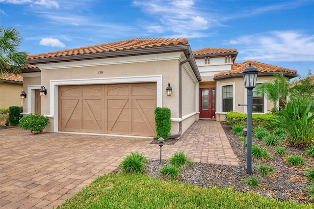 mediterranean / spanish home featuring an attached garage, stucco siding, decorative driveway, and a tile roof