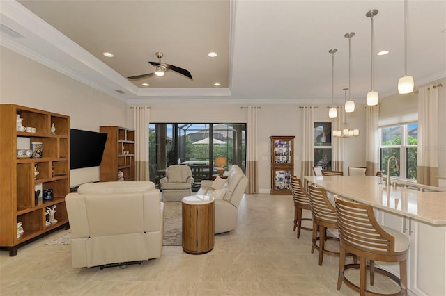 living room with ceiling fan with notable chandelier, plenty of natural light, sink, and ornamental molding