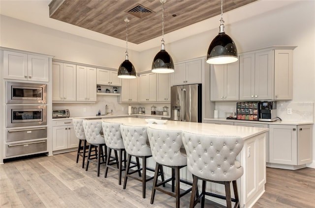 kitchen with stainless steel appliances, a breakfast bar, decorative light fixtures, light hardwood / wood-style flooring, and a center island