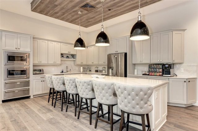 kitchen with stainless steel appliances, a warming drawer, a kitchen island, light countertops, and wood ceiling