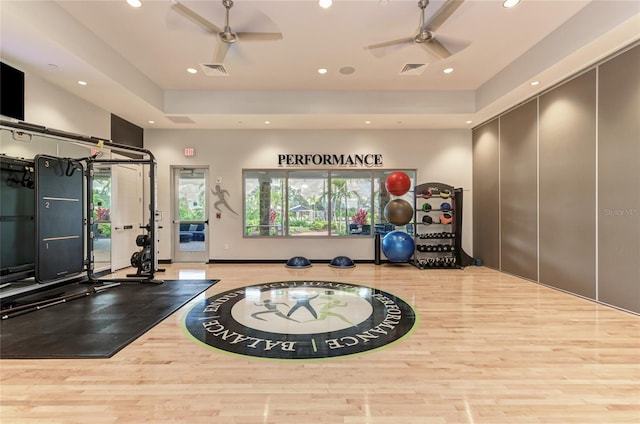 exercise room featuring a ceiling fan, recessed lighting, wood finished floors, plenty of natural light, and a tray ceiling