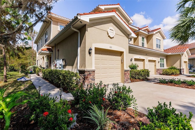 mediterranean / spanish house with a garage, stone siding, a tile roof, and stucco siding