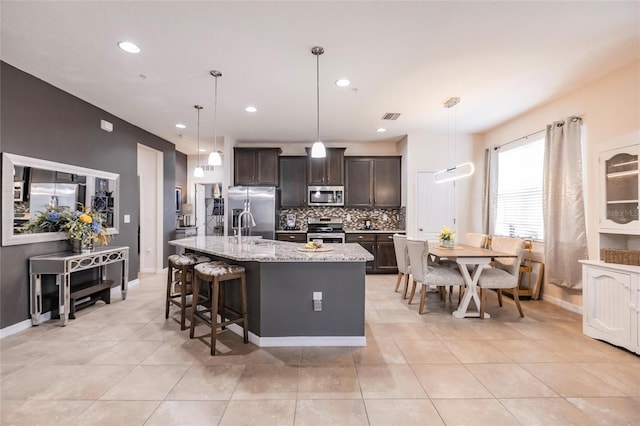 kitchen featuring visible vents, dark brown cabinets, appliances with stainless steel finishes, backsplash, and a center island with sink