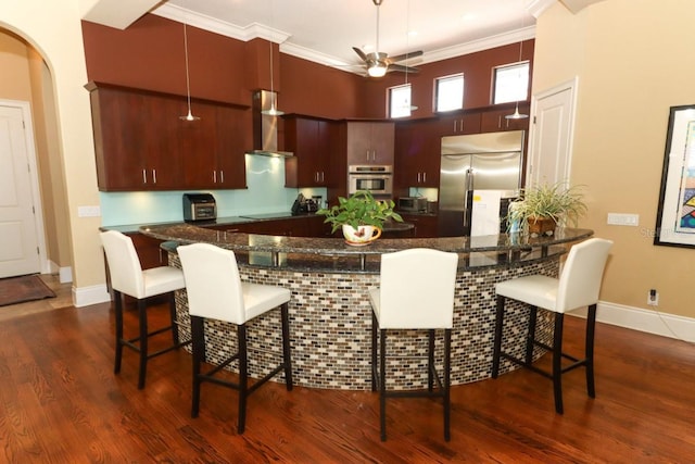 kitchen featuring wall chimney range hood, appliances with stainless steel finishes, dark hardwood / wood-style flooring, a breakfast bar, and kitchen peninsula