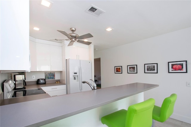 kitchen featuring white cabinetry, white fridge with ice dispenser, black range oven, light hardwood / wood-style flooring, and kitchen peninsula