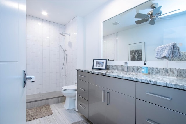 bathroom with vanity, ceiling fan, a tile shower, and toilet