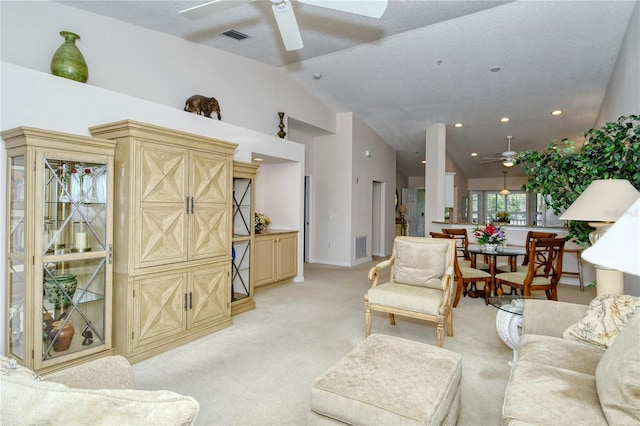 living room with ceiling fan, a textured ceiling, high vaulted ceiling, and light colored carpet