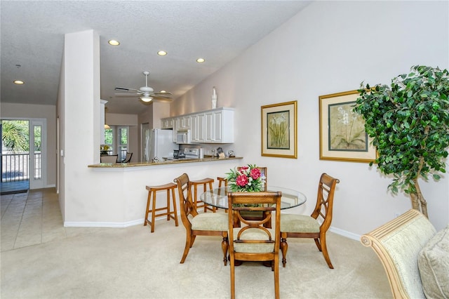 carpeted dining space with a textured ceiling, high vaulted ceiling, and ceiling fan