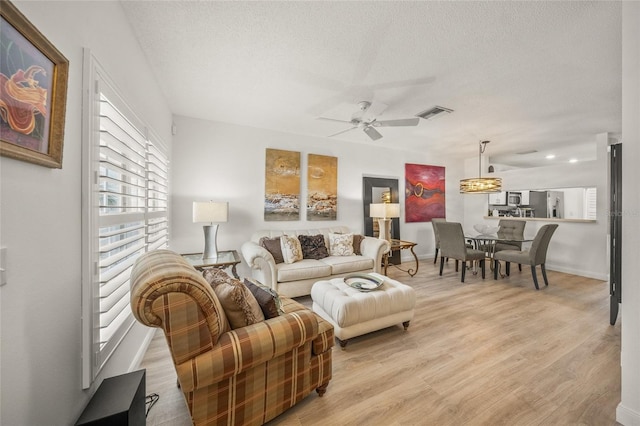 living room featuring a textured ceiling, light hardwood / wood-style flooring, and ceiling fan