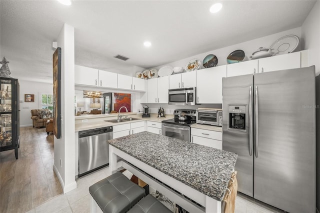 kitchen featuring a center island, sink, white cabinetry, light wood-type flooring, and appliances with stainless steel finishes