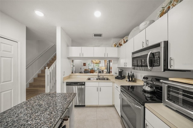 kitchen featuring dark stone counters, sink, light tile patterned floors, white cabinetry, and appliances with stainless steel finishes