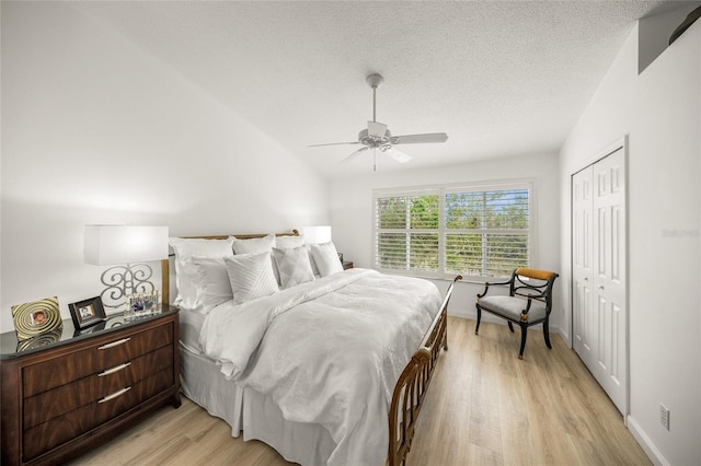 bedroom with a closet, a textured ceiling, vaulted ceiling, ceiling fan, and light hardwood / wood-style flooring