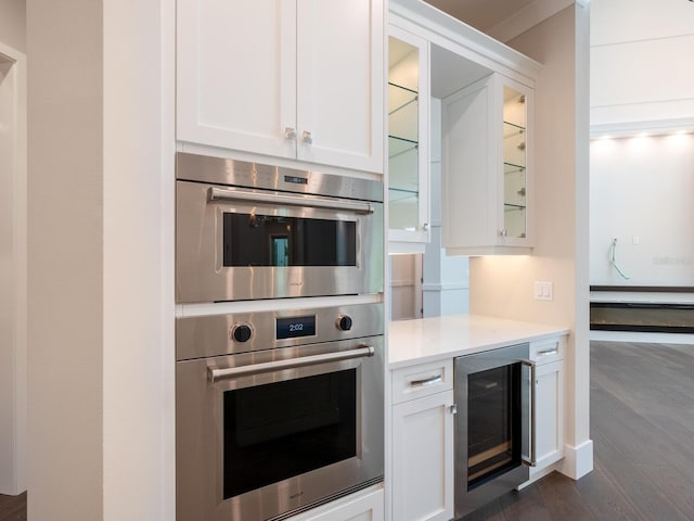 kitchen featuring double oven, dark hardwood / wood-style floors, white cabinetry, and wine cooler