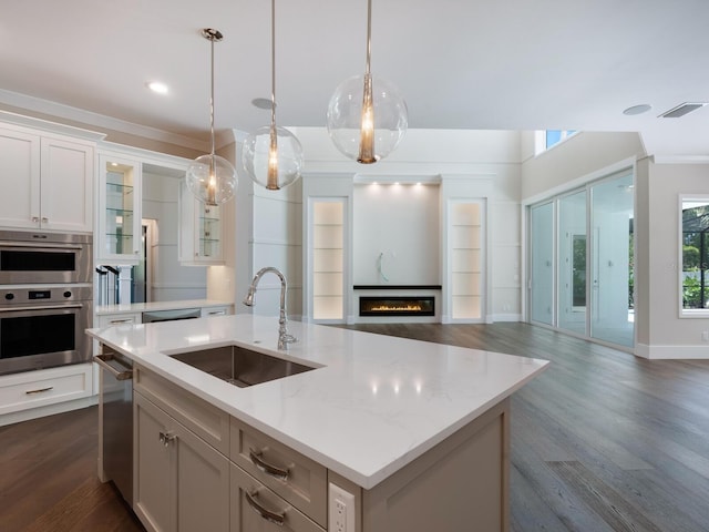 kitchen with sink, stainless steel appliances, dark wood-type flooring, decorative light fixtures, and a center island with sink