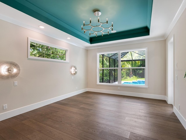 spare room with a raised ceiling, a chandelier, dark hardwood / wood-style flooring, and a healthy amount of sunlight