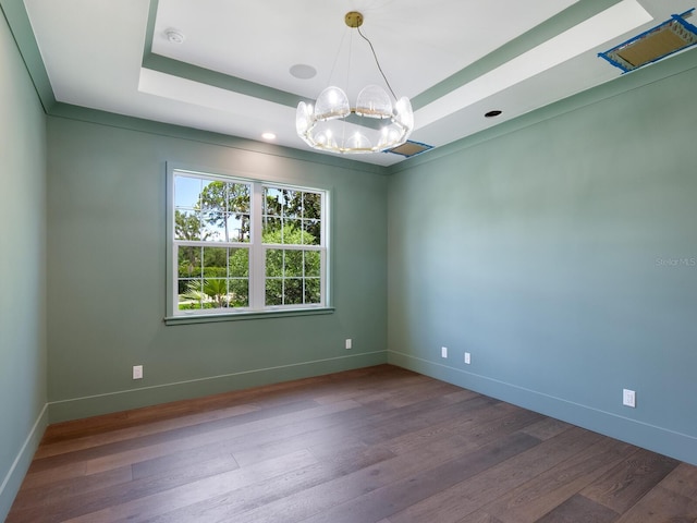 unfurnished room with a tray ceiling, wood-type flooring, and a notable chandelier