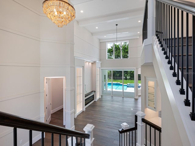 stairway featuring beamed ceiling, wood-type flooring, a high ceiling, and an inviting chandelier