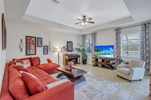 living room with a raised ceiling, ceiling fan, and light tile patterned flooring