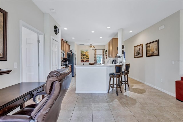 kitchen featuring kitchen peninsula, appliances with stainless steel finishes, a breakfast bar, ceiling fan, and light tile patterned flooring