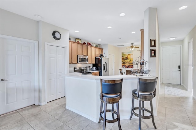 kitchen featuring ceiling fan, kitchen peninsula, a kitchen bar, light tile patterned flooring, and appliances with stainless steel finishes