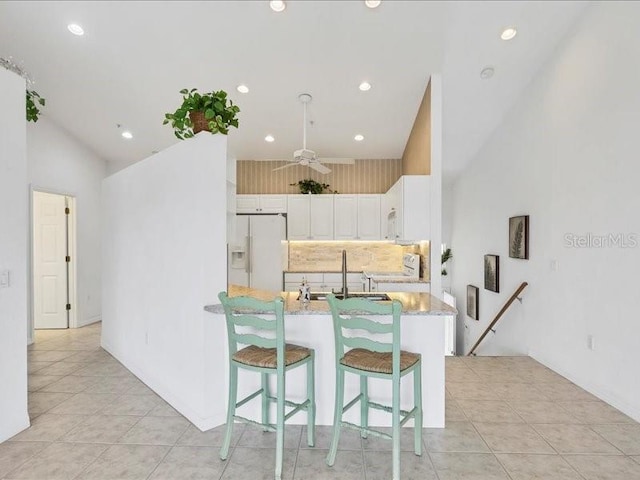 kitchen with white appliances, a kitchen breakfast bar, ceiling fan, light stone countertops, and white cabinetry