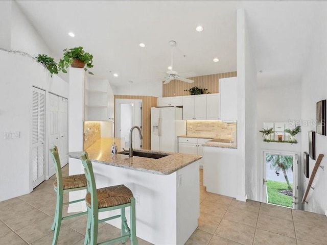 kitchen featuring white cabinetry, sink, white refrigerator with ice dispenser, kitchen peninsula, and a kitchen bar