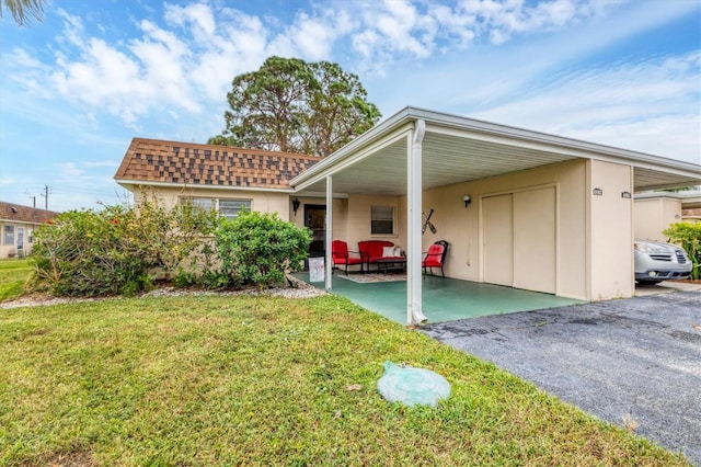 rear view of property with a yard, an attached carport, a shingled roof, and asphalt driveway