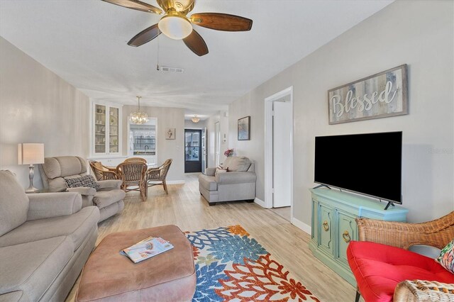 living room with light wood finished floors, a chandelier, a ceiling fan, and baseboards