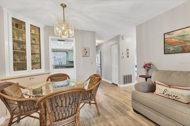 dining space with a textured ceiling, light hardwood / wood-style flooring, sink, and an inviting chandelier