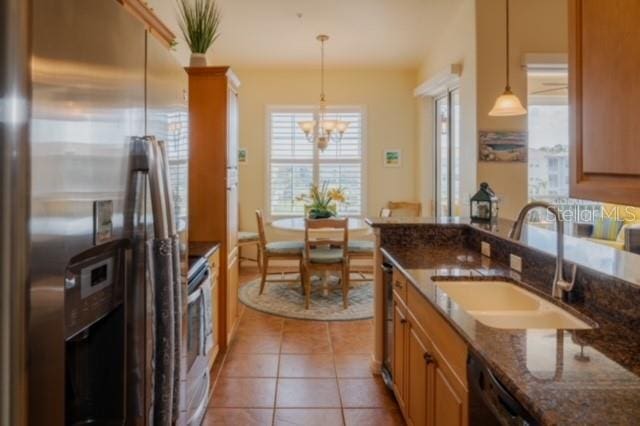 kitchen with pendant lighting, sink, dark stone countertops, appliances with stainless steel finishes, and a notable chandelier