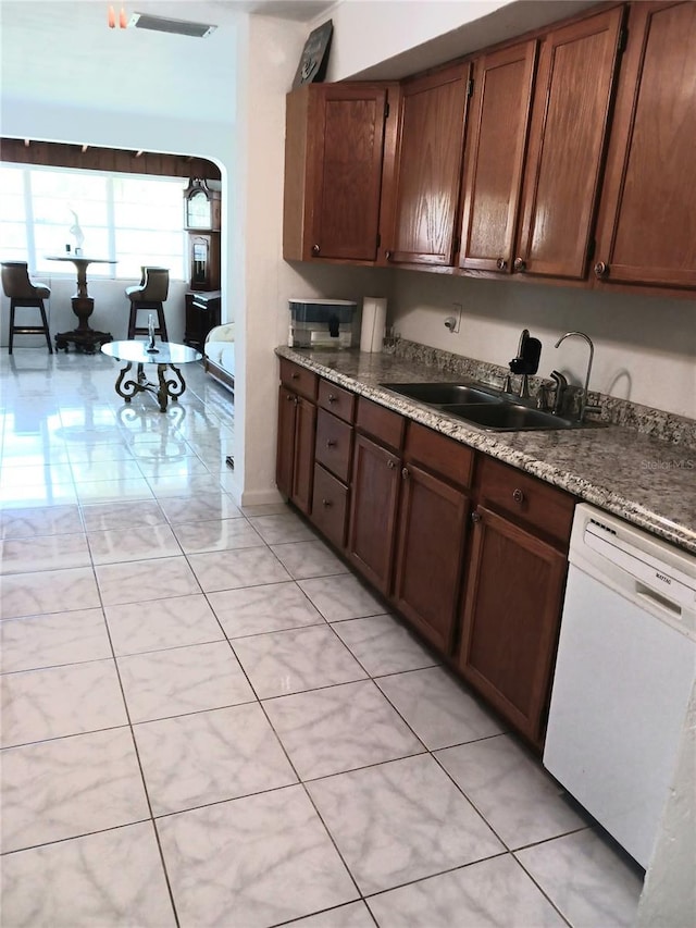 kitchen with light tile patterned flooring, white dishwasher, dark stone countertops, and sink