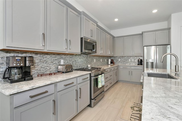 kitchen featuring stainless steel appliances, sink, light stone counters, gray cabinets, and decorative backsplash