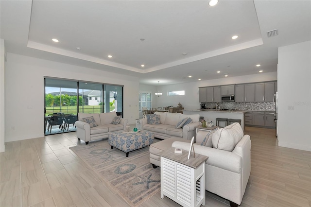 living room featuring sink, an inviting chandelier, and a tray ceiling