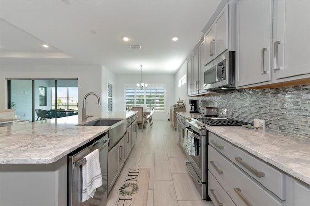 kitchen with sink, backsplash, stainless steel appliances, and a center island with sink