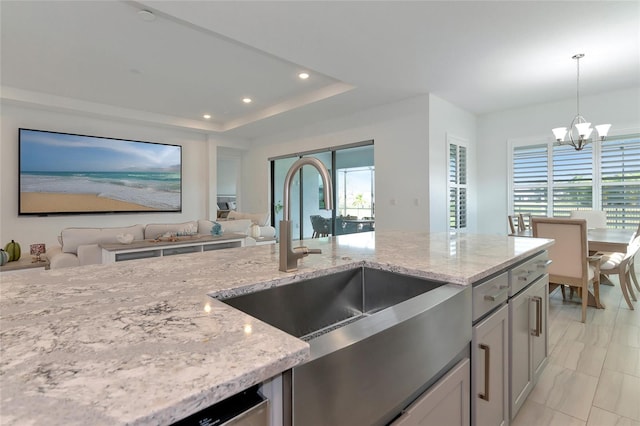 kitchen featuring pendant lighting, sink, a chandelier, a tray ceiling, and light stone countertops