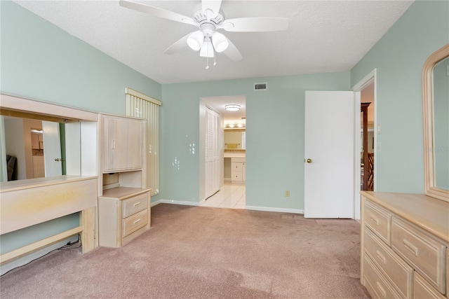 unfurnished bedroom featuring a textured ceiling, connected bathroom, light colored carpet, and ceiling fan