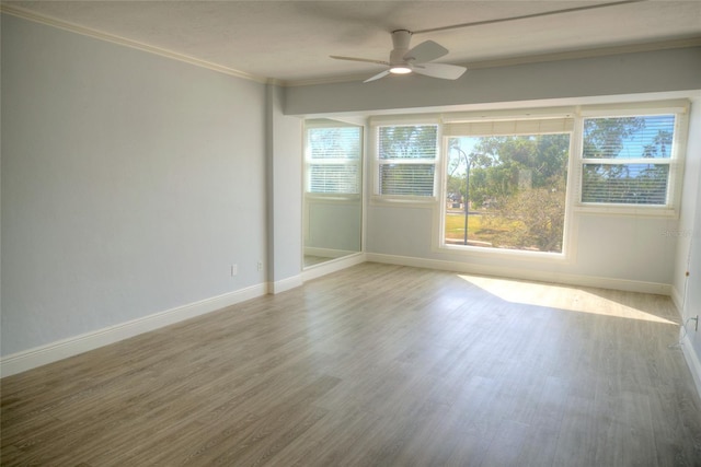 empty room with ceiling fan, wood finished floors, baseboards, and ornamental molding