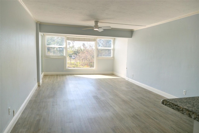 spare room with a ceiling fan, crown molding, wood finished floors, baseboards, and a textured ceiling