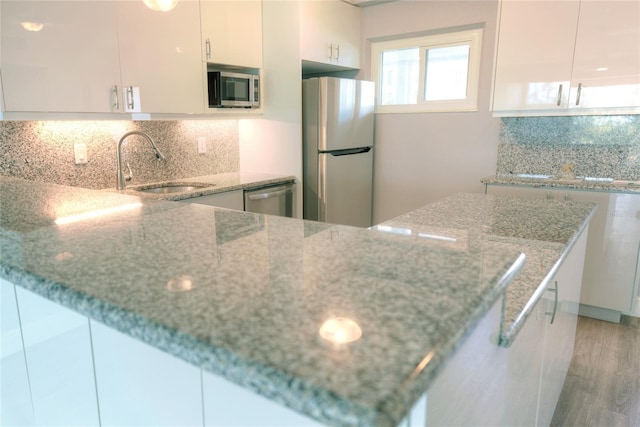 kitchen with appliances with stainless steel finishes, backsplash, light stone counters, sink, and white cabinetry