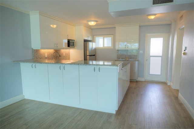 kitchen with backsplash, white cabinets, light wood-type flooring, appliances with stainless steel finishes, and kitchen peninsula