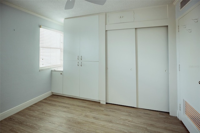 unfurnished bedroom with light wood-type flooring, crown molding, a closet, ceiling fan, and baseboards