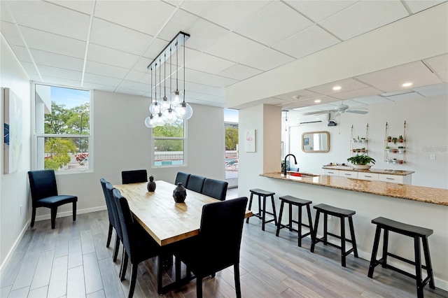 dining space with a wall unit AC, a paneled ceiling, sink, and plenty of natural light